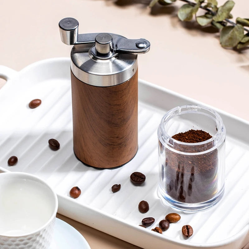 Wood-grain hand coffee grinder next to its clear acrylic catch jar filled with ground coffee
